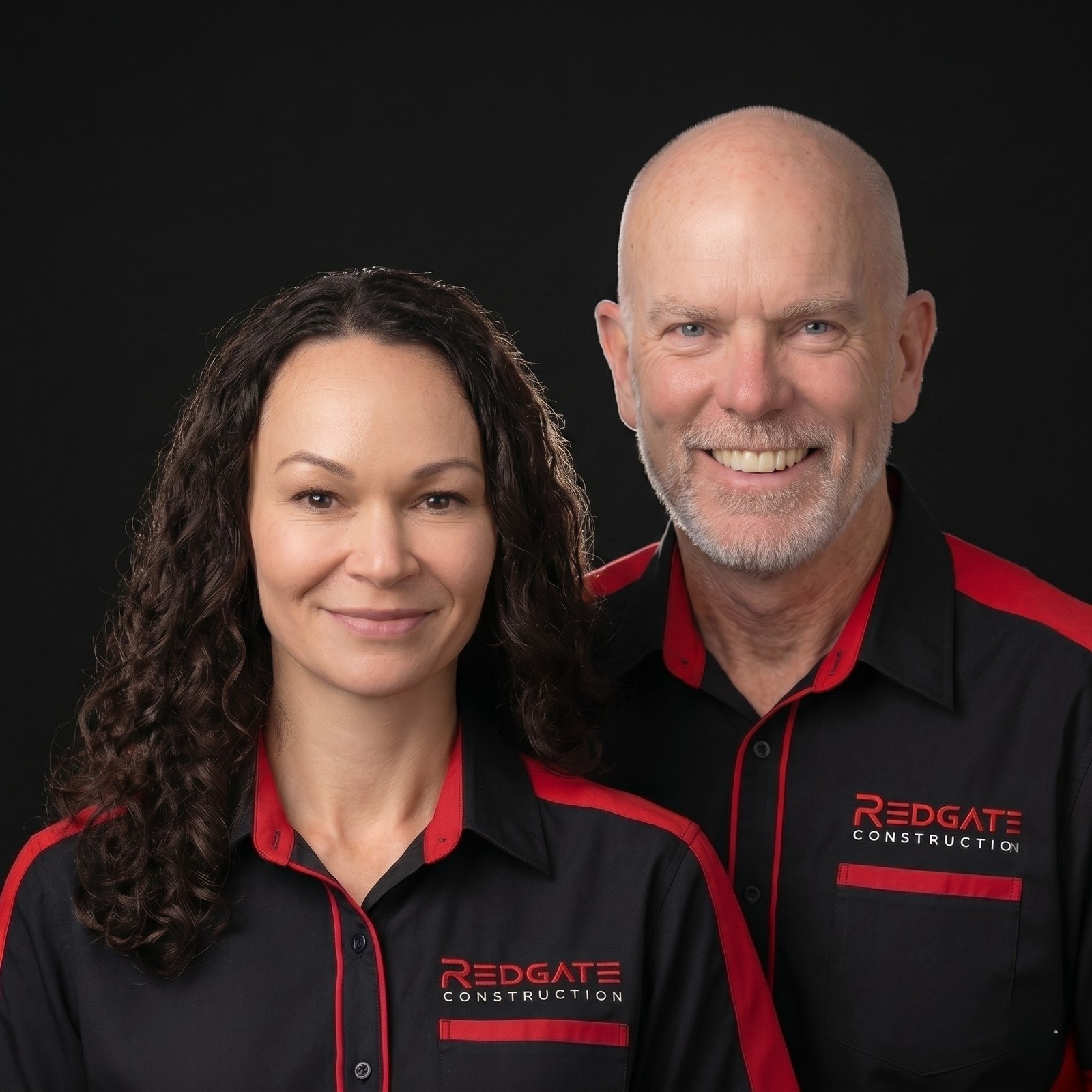 Eva Redgate and Grant Redgate, founders of Redgate Construction, wearing the brand uniform on a dark studio background